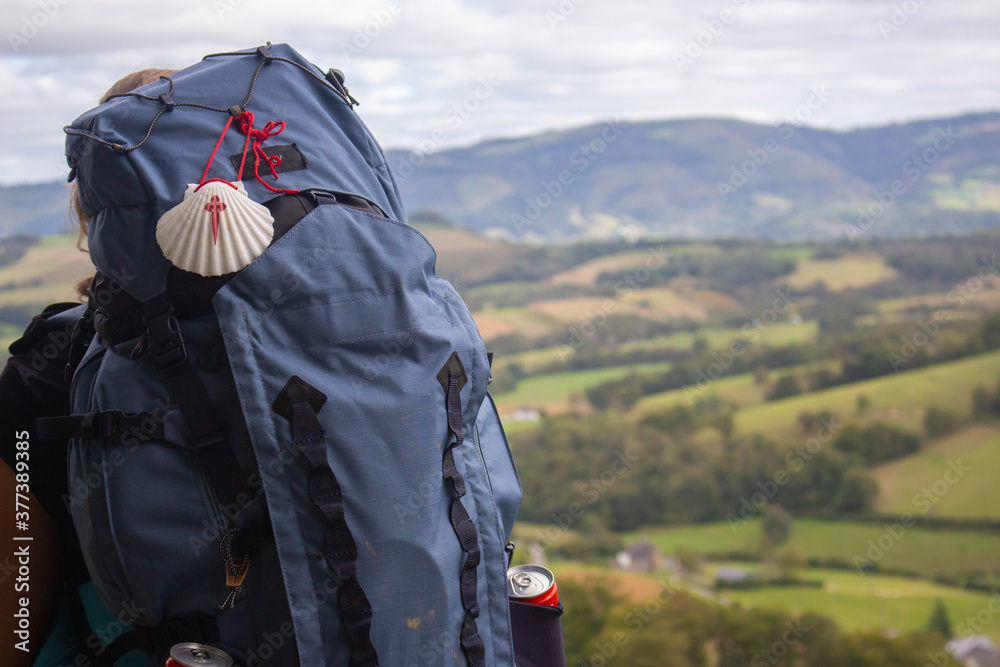 Big backpack with pilgrim shell on mountain background. Pilgrimage concept. Pilgrim on Camino de Santiago road. Tourist with rucksack on beautiful landscape background. Religious travel.