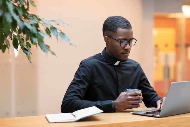 Young male priest using laptop at a cafe | Free Photo